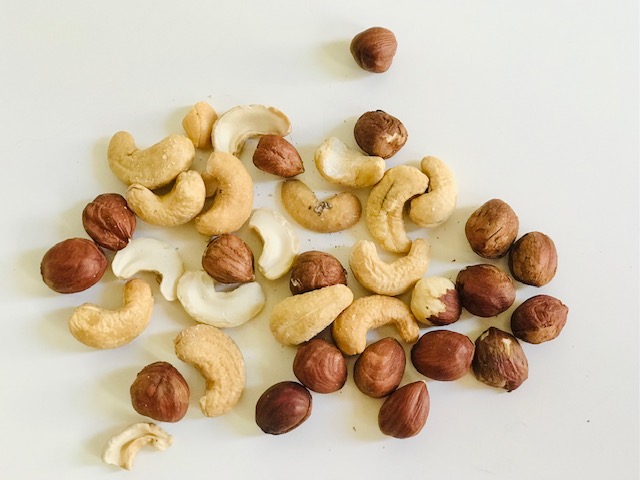 Haselnüsse und Cashewnüssen liegen zusammengemischt auf einem weißen Untergrund