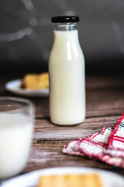 eine Glasflasche und ein noch gerade sichtbares Glas mit Milch steht auf einem ländlichen dekorierten Holztisch