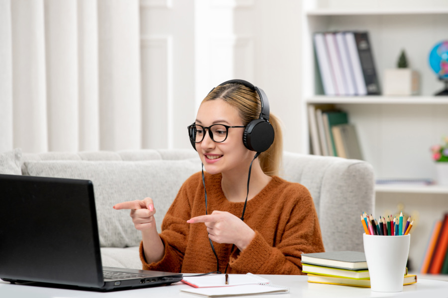 Studentin online mit Brille und Pullover, das lächelnd am Computer studiert