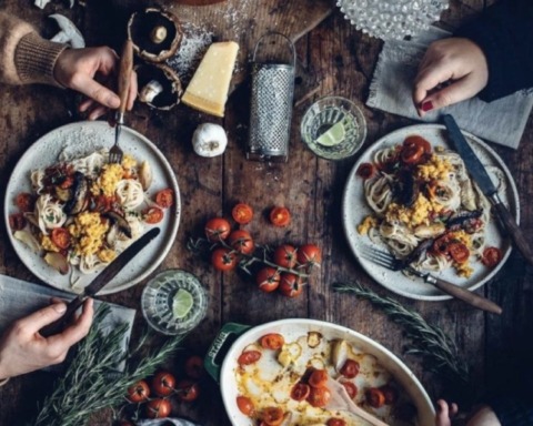 Zwei Menschen sitzen an einem köstlich mit Essen gefüllten Tisch und essen gemainsam.