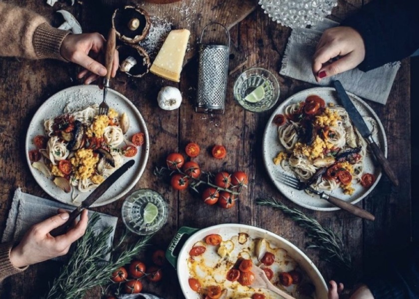 Zwei Menschen sitzen an einem köstlich mit Essen gefüllten Tisch und essen gemainsam.