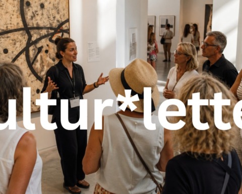 Eine Gruppe von acht Erwachsenen nimmt an einer Führung durch eine moderne Kunstausstellung teil. Eine Museumsführerin erklärt vor einem großformatigen abstrakten Gemälde ein Kunstwerk, während die Besucher aufmerksam zuhören. Der helle Ausstellungsraum ist lichtdurchflutet und vermittelt eine ruhige, sommerliche Atmosphäre.