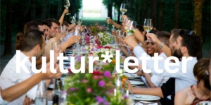 Viele Menschen sitzen an einer Sommertafel und feiern bei einen Abendessen. Dabei prosten sie sich zu.