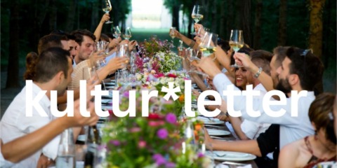 Viele Menschen sitzen an einer Sommertafel und feiern bei einen Abendessen. Dabei prosten sie sich zu.