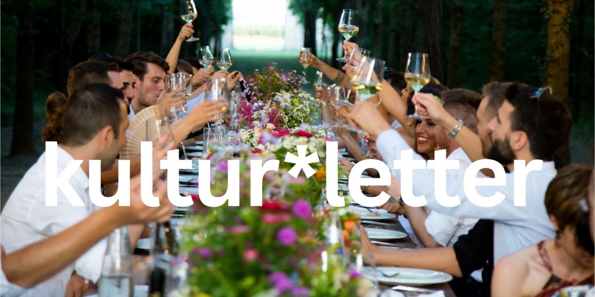 Viele Menschen sitzen an einer Sommertafel und feiern bei einen Abendessen. Dabei prosten sie sich zu.
